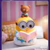 A cute bear figure sits atop a yellow, round character with large glasses and a pink book, displayed as a blind box collectib