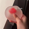 A hand holds a pink strawberry mochi squishy stress relief toy against a dark background.