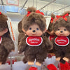 A collection of brown Monchhichi plush toys hanging by their ears, featuring red bows and round tags.