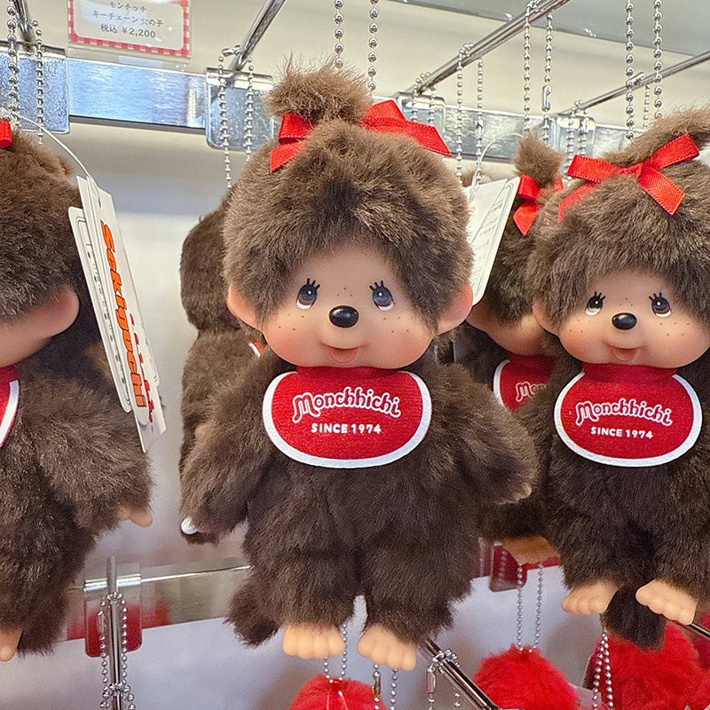 A collection of brown Monchhichi plush toys hanging by their ears, featuring red bows and round tags.