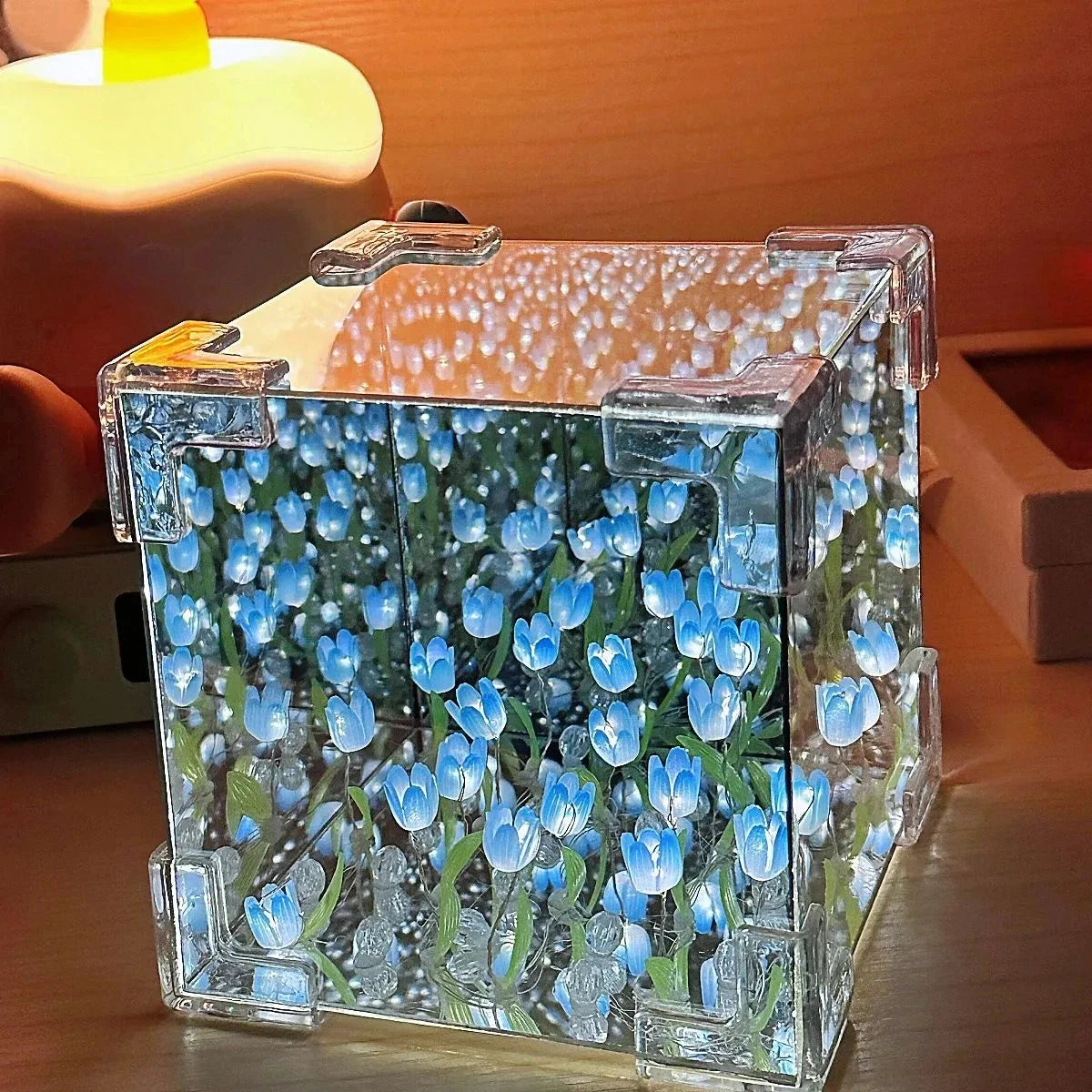 A clear glass cube filled with blue and white faux tulips, used as a night light or craft item.
