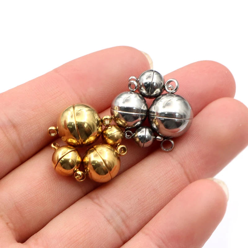 A hand holds a cluster of round stainless steel magnetic clasps in gold and silver finishes.