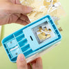 A hand holds a blue DIY puzzle making tool containing a small piece of paper with a bird design.