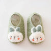 Pair of soft, light green plush baby slippers with white bunny ears and anti-slip soles