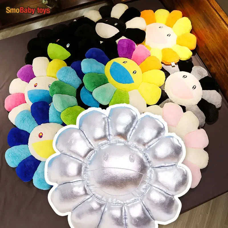 A large, silver-colored sunflower plush cushion with a cheerful design is shown on a dark surface.