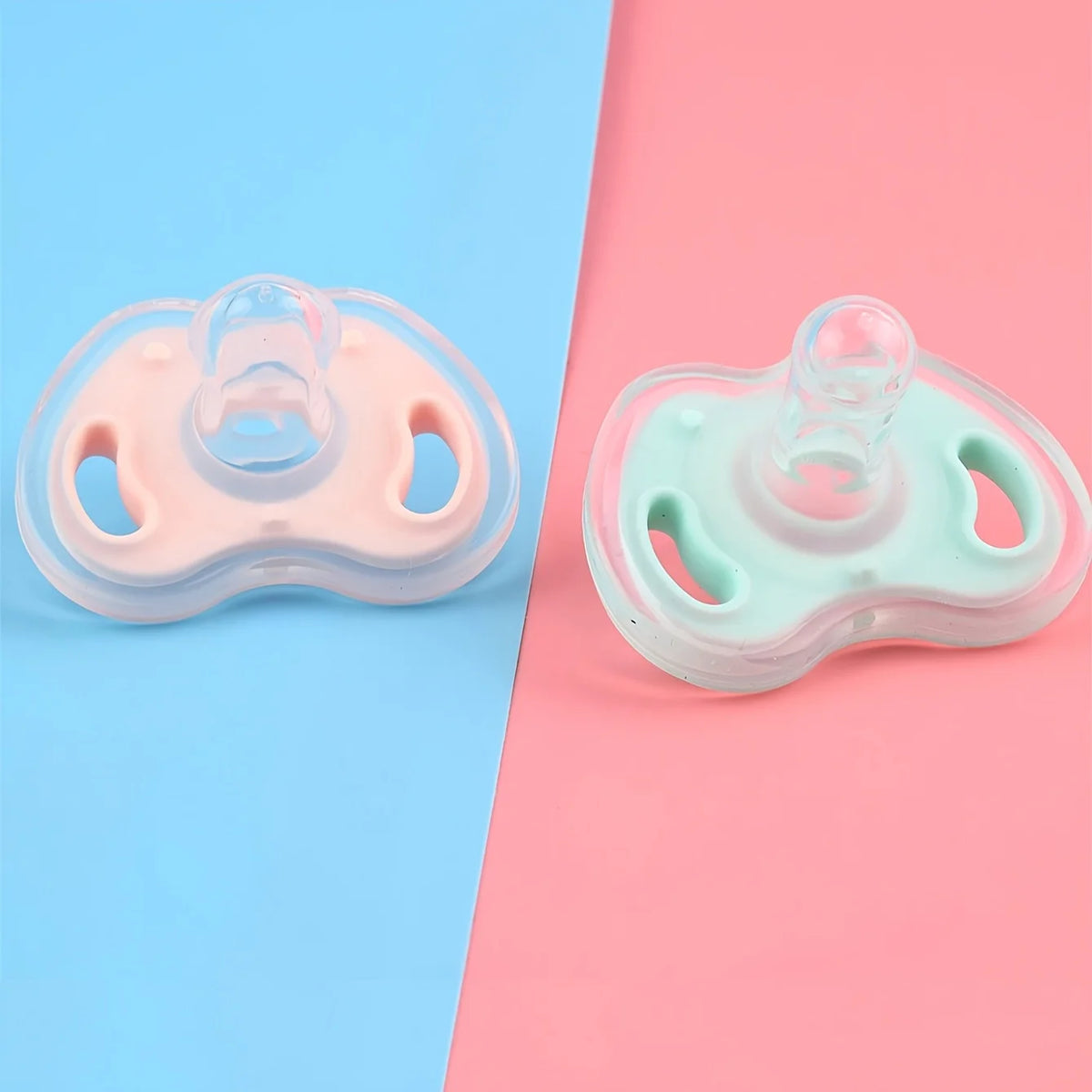 A soft silicone baby pacifier in pink and mint green is shown on a light blue and pink background.