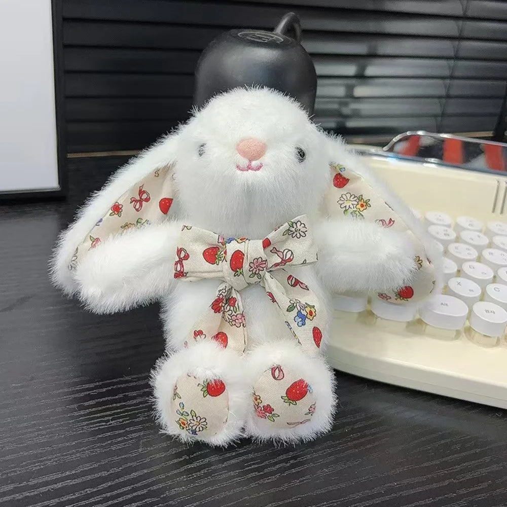 A white bunny plush toy with a floral bow charm sitting next to a silver tray.