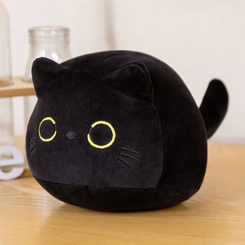 A round, black plush cat with yellow eyes is shown on a wooden surface.