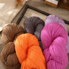 A collection of brightly colored wool yarn skeins in shades of orange, pink, and gray are displayed on a wooden surface.