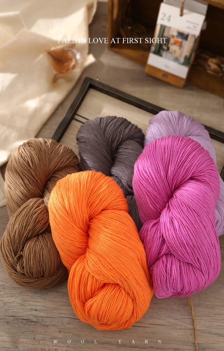 A collection of brightly colored wool yarn skeins in shades of orange, pink, and gray are displayed on a wooden surface.
