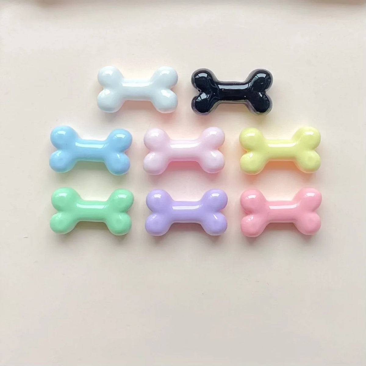 A collection of nine small, cute resin bone charms in various pastel colors like blue, black, pink, and yellow.