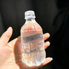 A hand holds a clear plastic water bottle squishy toy against a dark background.