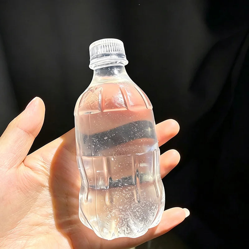A hand holds a clear plastic water bottle squishy toy against a dark background.