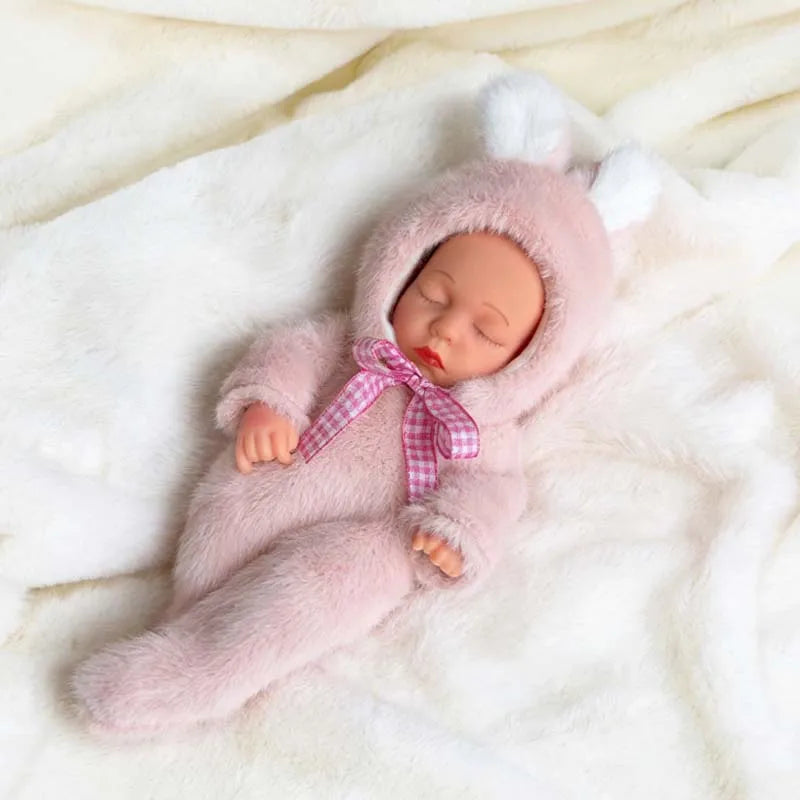 A realistic soft vinyl baby doll wearing a pink fuzzy outfit and hood, lying on white fur fabric.
