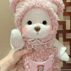 A pink fluffy teddy bear plush toy wearing a white dress and a pink hood.