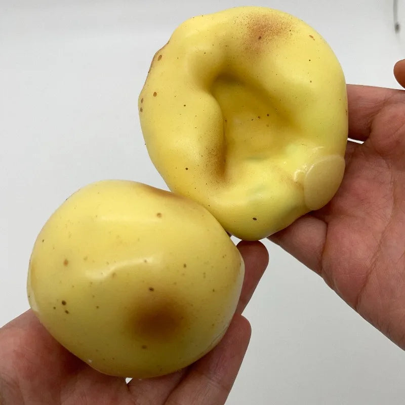 A hand holds a yellow, squishy potato stress ball fidget toy with brown discoloration.