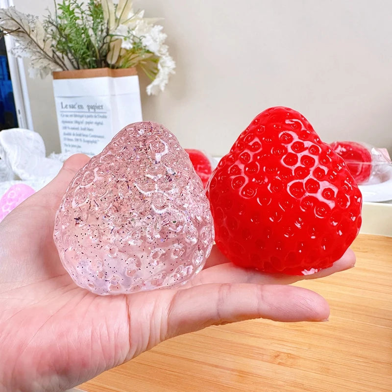 A hand holds a pink glitter strawberry squishy fidget toy against a light background.