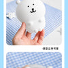 A hand holds a white silicone lamp shaped like a bear, showing the charging port and battery indicator light.