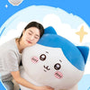 A white and blue Chiikawa plush doll is shown resting on a light-colored surface, with a person gently holding it.