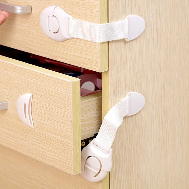 A close-up of a child safety cabinet lock set with white plastic latches and hardware on a light wood cabinet.