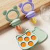 A silicone baby fruit feeder set with purple and green molds and feeding tubes resting on a wooden surface.