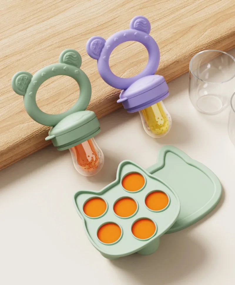 A silicone baby fruit feeder set with purple and green molds and feeding tubes resting on a wooden surface.