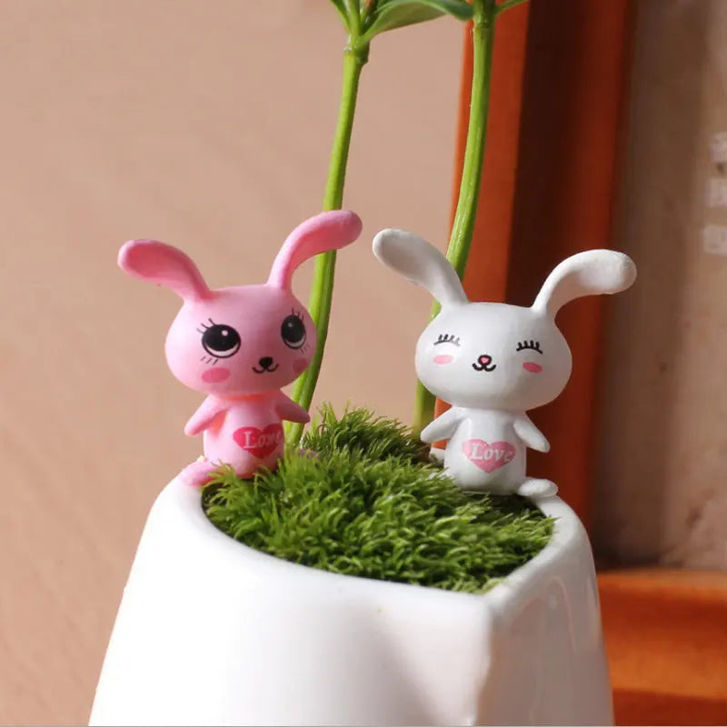 Two pink and white rabbit figurines growing out of green moss in a white pot