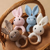 A set of handmade crochet bunny rattles in pink, blue, and white yarn displayed in a woven basket.