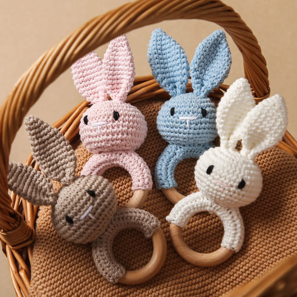 A set of handmade crochet bunny rattles in pink, blue, and white yarn displayed in a woven basket.