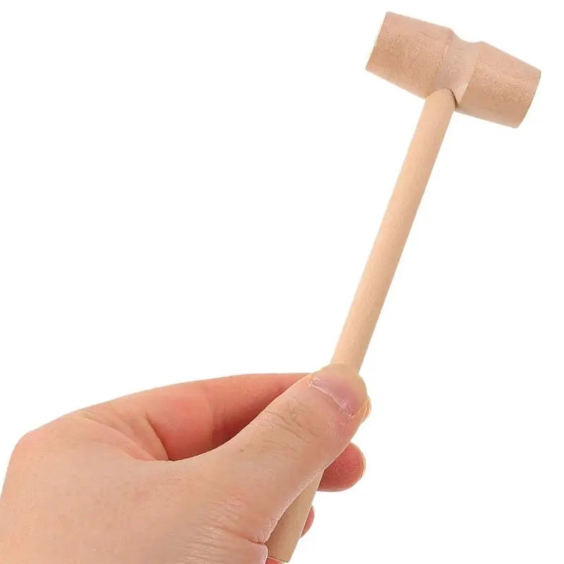 A hand holds a wooden hammer used in a dinosaur excavation kit for young archaeologists.
