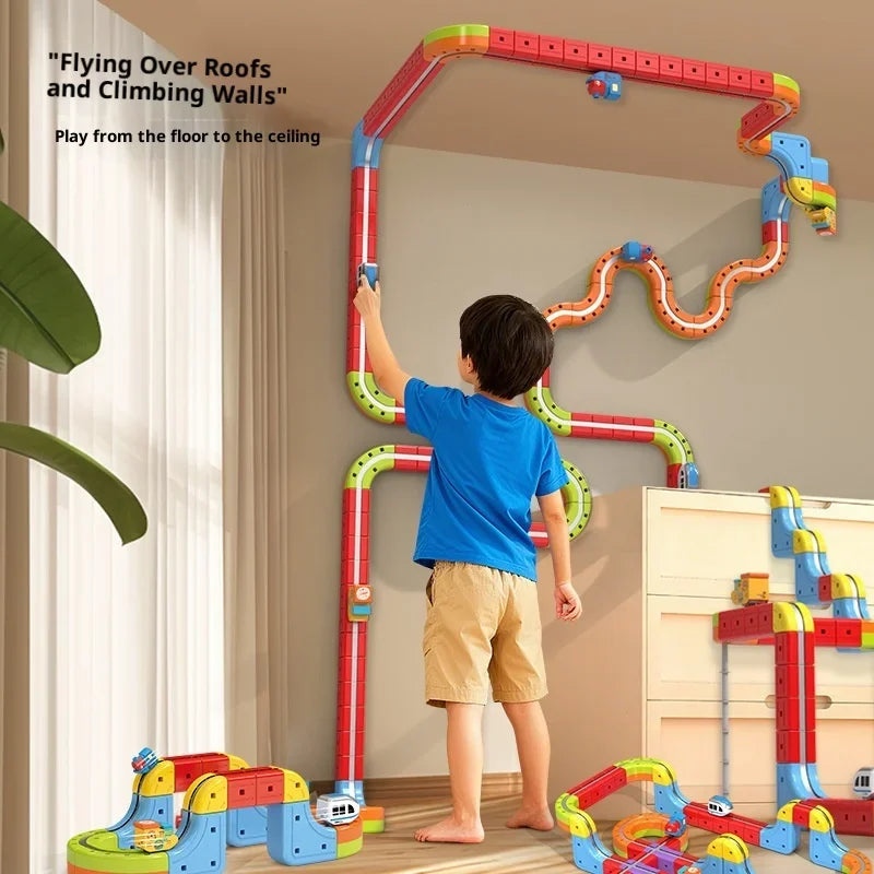 A boy is playing with a red and green magnetic anti-gravity train track set indoors.