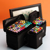 A set of alcohol markers in various colors is displayed in a black storage box with a wooden frame on an orange background.