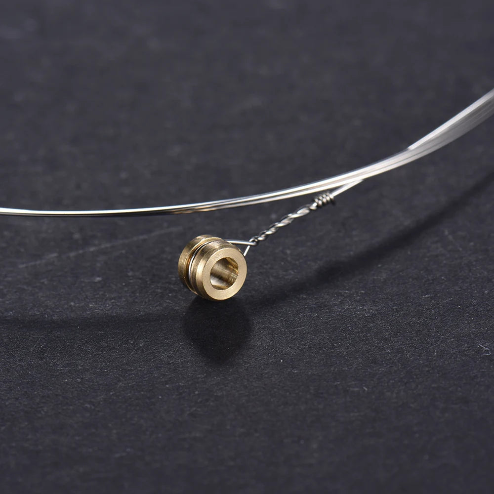 A close-up of a phosphor bronze acoustic guitar replacement string with a gold-colored nut and wire, lying on a dark surface.