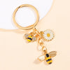Gold-toned enamel keychain featuring a bee and a daisy flower design.