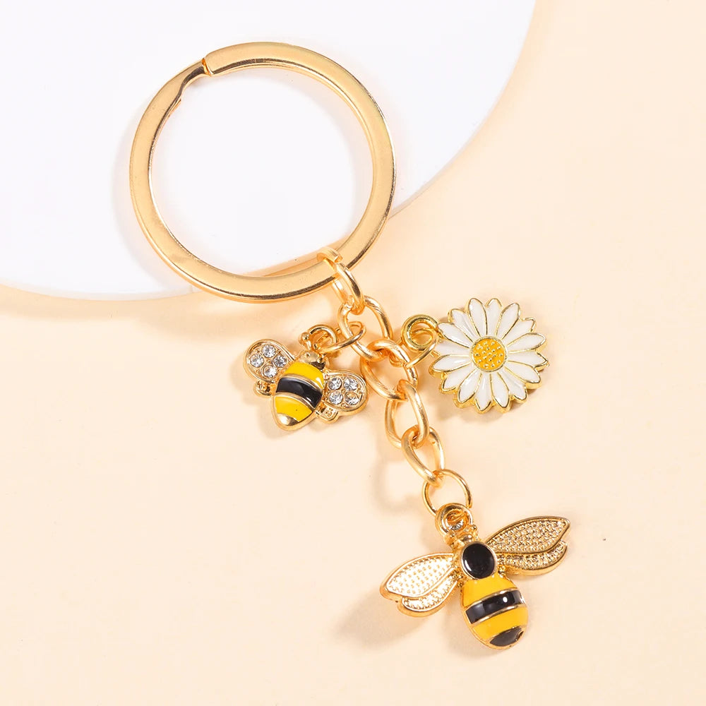 Gold-toned enamel keychain featuring a bee and a daisy flower design.