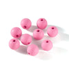 A collection of matte pink acrylic round beads with drilled holes scattered on a white background.