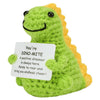 A handmade crochet dinosaur toy with a smiling face and yellow spines, holding a sign that reads Dino-mite.