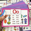 A hand holds a stack of purple alphabet flash cards featuring the letter Oo and various words for tracing practice.