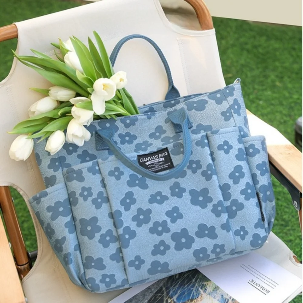 A light blue floral canvas tote bag with multiple pockets resting on a white chair outdoors.