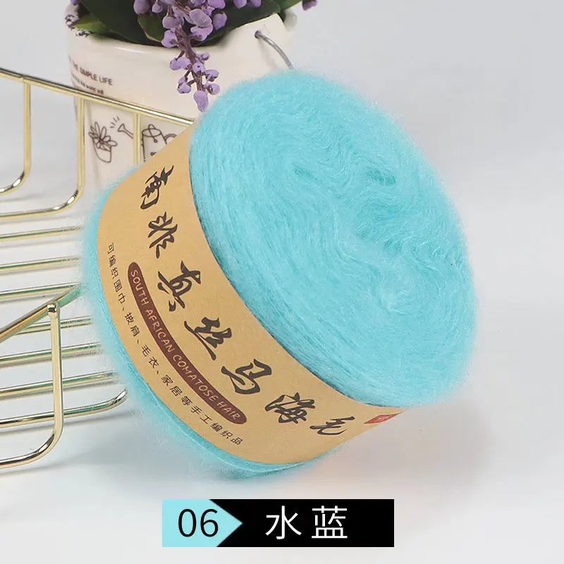 A ball of light blue fuzzy yarn labeled South African Comatose Hair for knitting projects