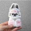 A light gray and pink cartoon animal plush keychain with large ears and a pink flower accessory being held in a hand.
