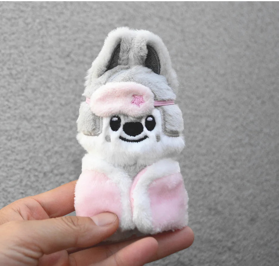 A light gray and pink cartoon animal plush keychain with large ears and a pink flower accessory being held in a hand.