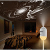 A white night light with a spherical lamp illuminates a bedroom ceiling projection of an angel with wings against a starry sk