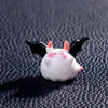 A white cartoon pumpkin bear figurine with pink ears and black wings displayed on a dark surface.