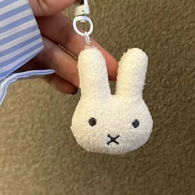 A white, fluffy Miffy cartoon rabbit keychain pendant is being held by a hand.