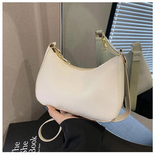 A light beige PU square crossbody bag with a gold zipper closure is held against a blurred background.