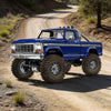 A blue Ford pickup truck is parked on a dirt road with large off-road tires.