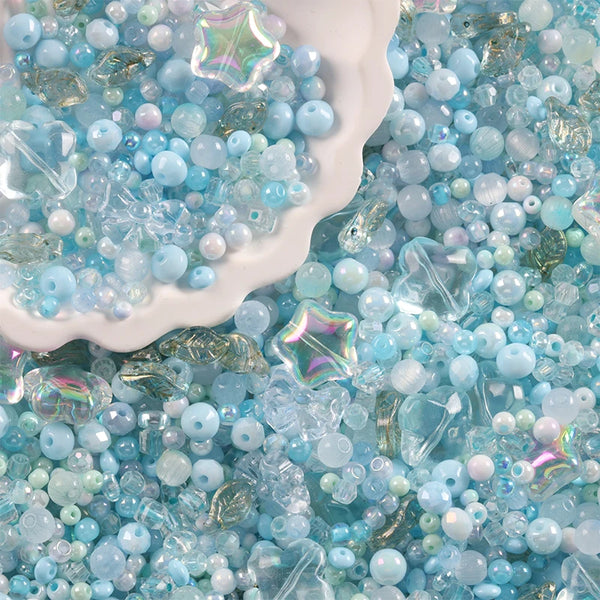 Gros plan de perles de verre bleues et claires mélangées éparpillées sur un plat blanc.