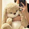 Un ours en peluche lapin géant beige clair et en colère tenu par la main d'une personne.