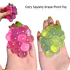 A hand is holding a colorful squishy grape pinch toy with translucent pink and green fruit shapes.